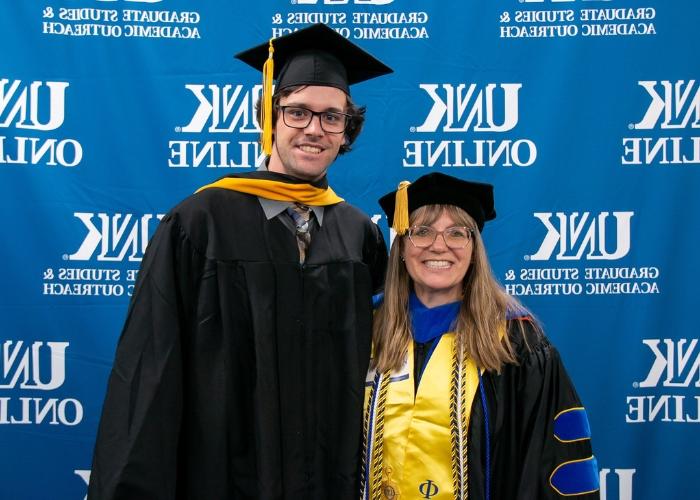 Professor and graduate pose in cap and gown.